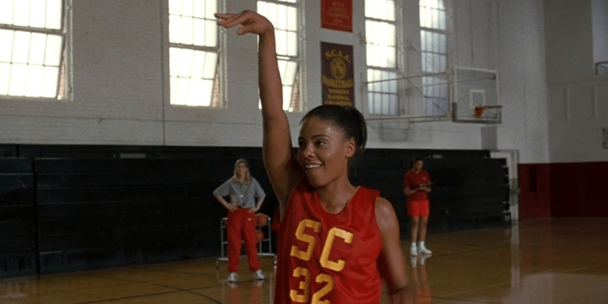 Image shows Sanaa Lathan portraying Monica and she is in the middle of a basketball court wearing a jersey and doing her infamous hand gesture after shooting the basketball with a smile