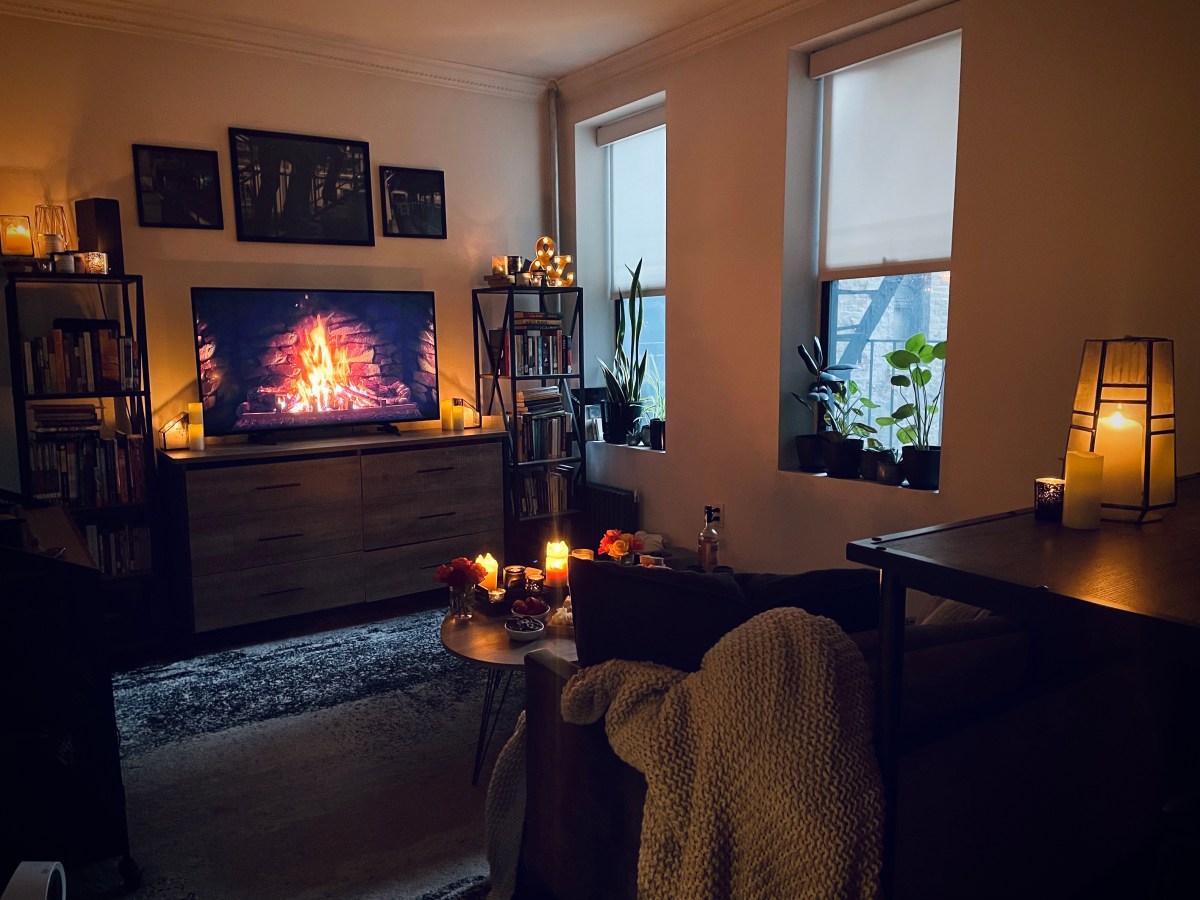 a candlelit room set up for holiday date night with a fireplace on the television, and throw blanket visible on the corner of the couch