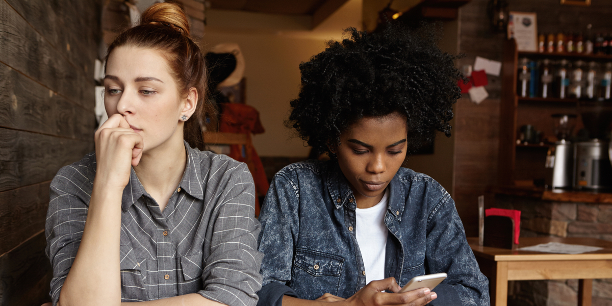 Two women sitting at a coffee shop, not looking at each other