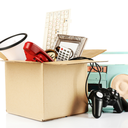 A cardboard box contains a megaphone, a keyboard, a mirror and other items. Beside the box, there is a video game controller and a light blue boom box.