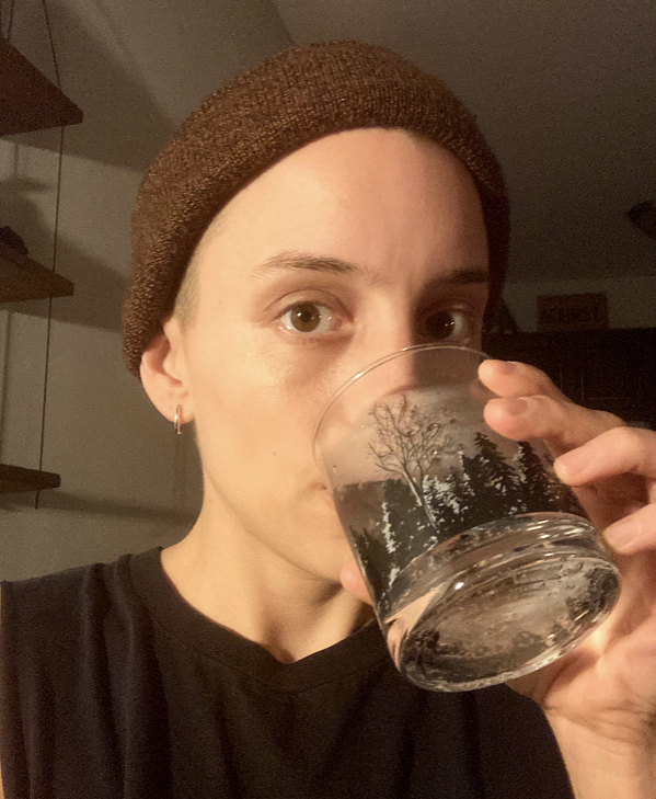 Ro is drinking water out of a foresty-patterned glass. Ro is wearing a beanie.