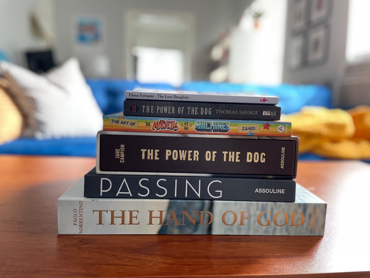 Books Riese got in the mail from Netfilx in a stack: The Hand of God, Passing, The Power of the Dog, The Mitchells vs the Machines, The Power of the Dog novel and The Lost Daughter