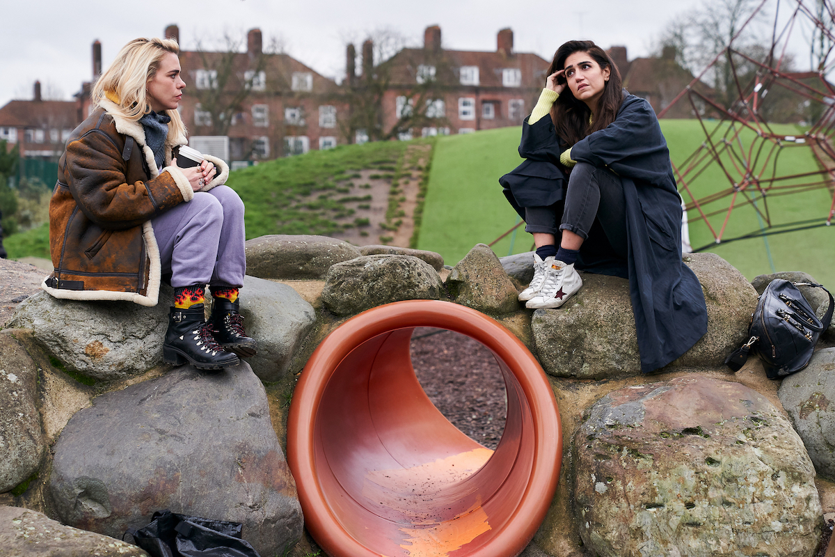 Suzie and Naomi sitting in a park looking upset 