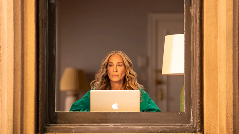 Carrie sits at her computer in front of the window. 