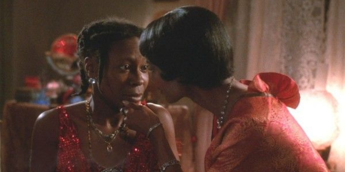 Shug has her fingers resting on Celie's chin, lifting her face upwards gently while Celie curiously stares at her.