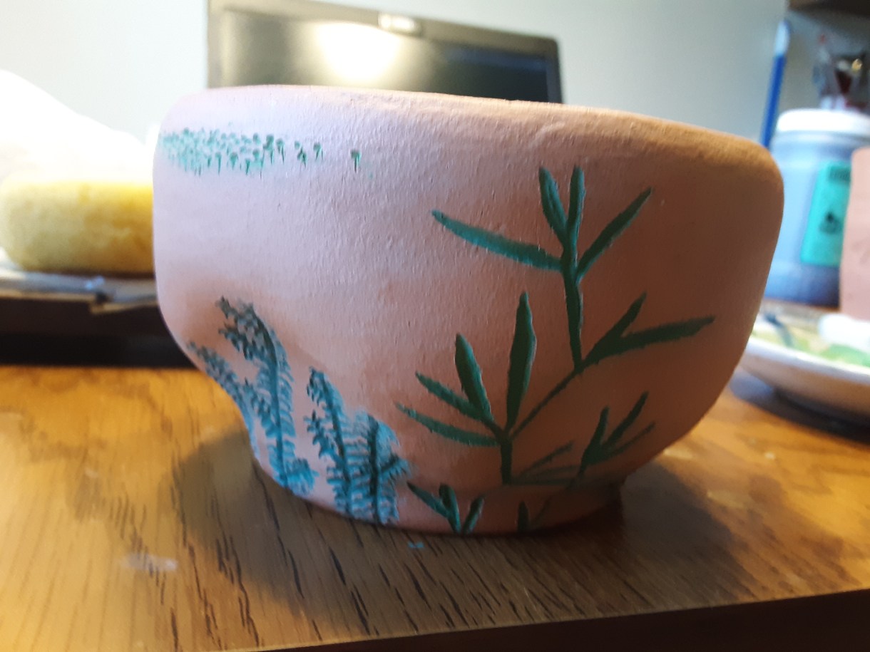 a little pink ceramic bowl with various green plant patterns on it. It has an impression in it so that it can be perfectly held in the hand.