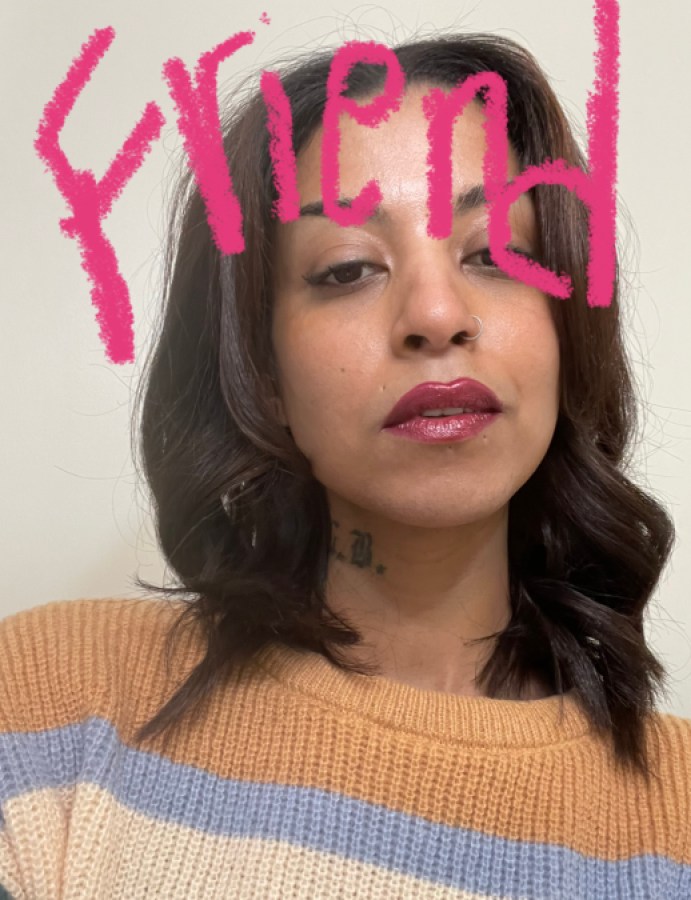 This is a photo of Lauralee Benjamin. Lauralee is a Black woman with long wavy dark brown hair, a nose piercing, and a tattoo on her neck. She is wearing sparkling pink lipstick and a sweater. Across the top of the photo is written "Friend" in pink.