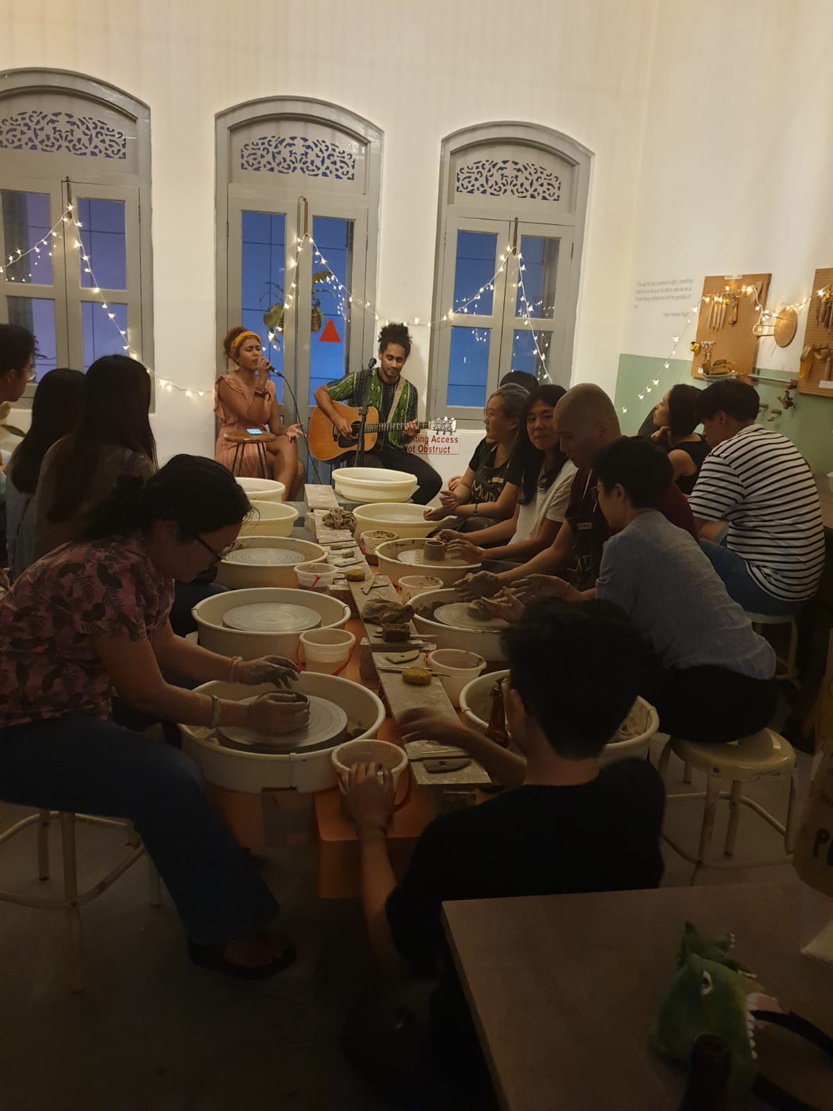 This is an image of a large group of people all working at clay at the same time while a guitarist and a singer play and sing in the background.