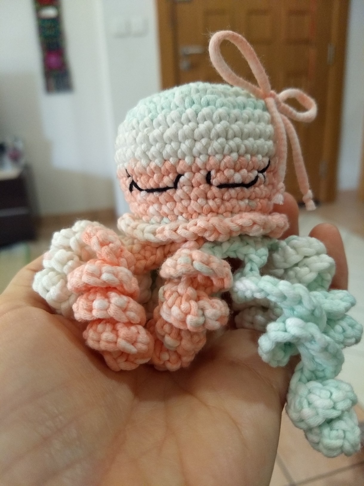 This little crocheted octopus has cute little eyes sewn on it. It's being held in the palm of a hand.