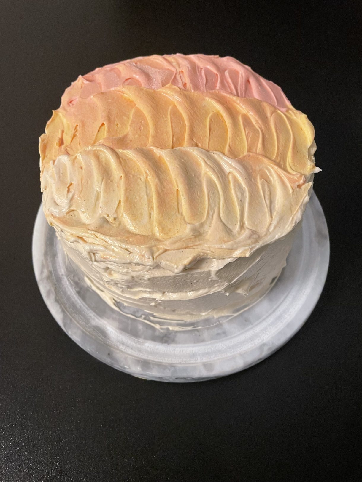 An ombre frosted cake in tones of pink, orange, and peach.