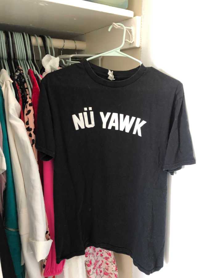A black tee shirt with the words NÜ YAWK in white on it. It is hanging in a closet.