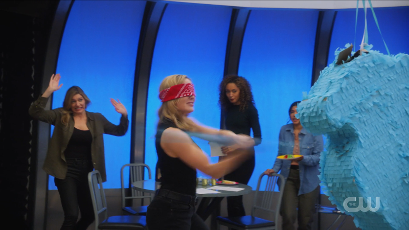 Sara is blindfolded and swinging a bat at Beebo, her muscles on full display thanks to a tank top