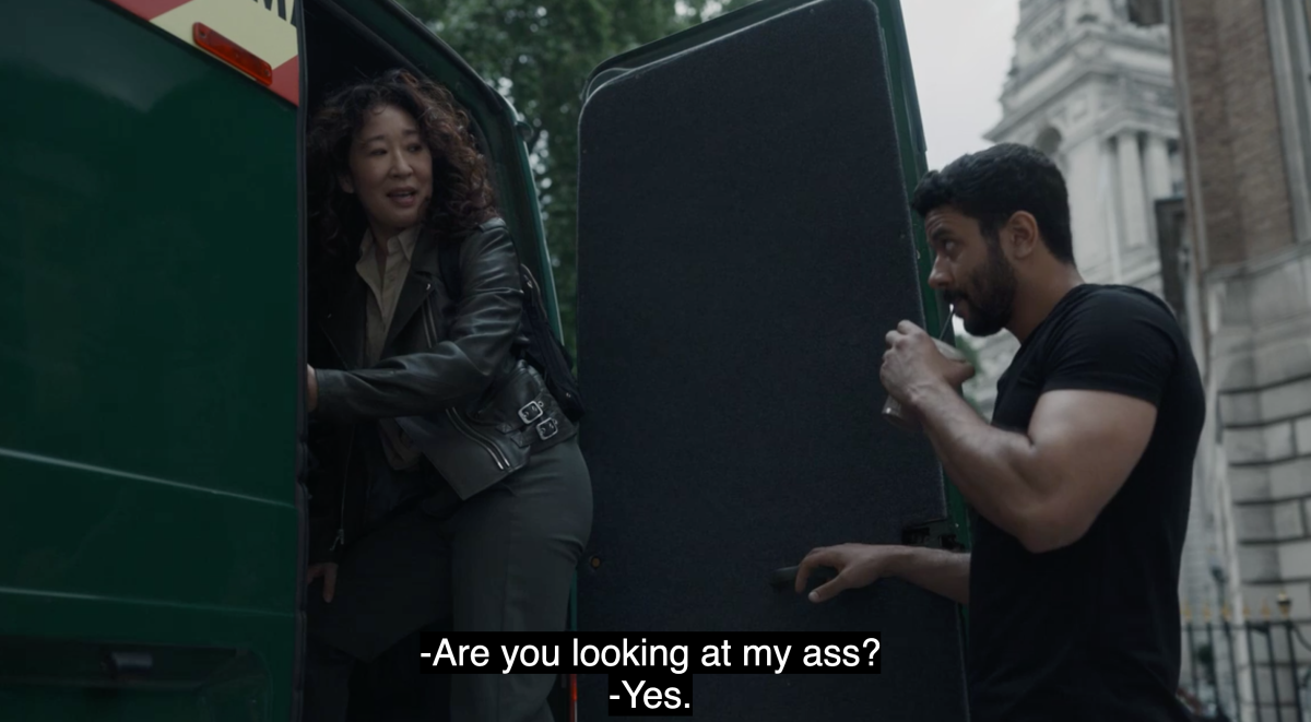 Eve (Sandra Oh) of Killing Eve wears a black moto jacket while getting into a van and turning back to look at Yusef, a man drinking a protein shake. Eve asks: Are you looking at my ass? Yusef says yes.