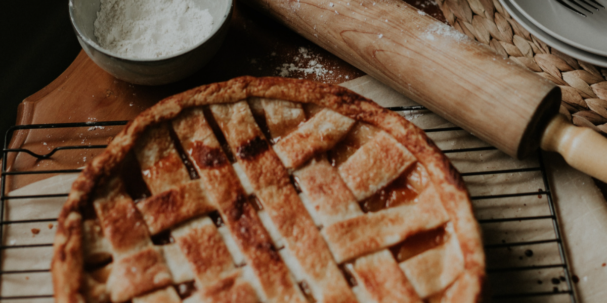 A perfectly baked pie rests on a table surrounded by a cup of flour and a rolling pin.