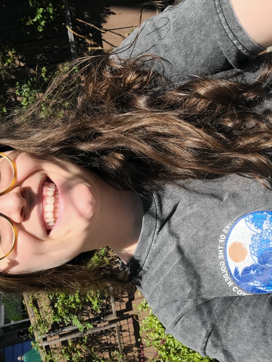 Anya, a white woman with glasses and long brown hair, is wearing a shirt with a little west coast looking graphic on it.