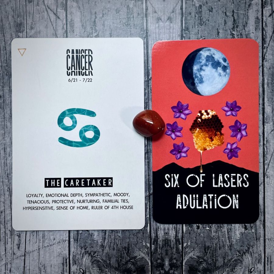 Six of Lasers Adulation is an orange cad with a collage of the moon and purple flowers, the card next to it is Cancer is the Caretaker