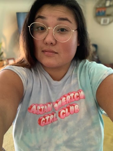 Em, an Asian human with long dark hair and glasses, is wearing a shirt that reads "Asian American Girl Club"