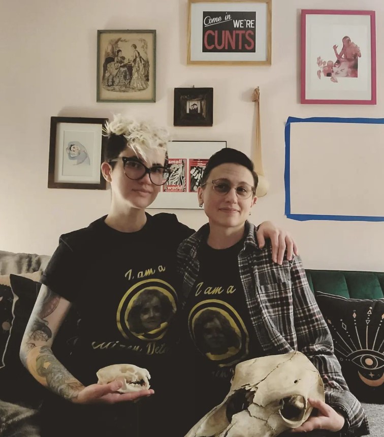 Nicole, a white human with shaved sides and bleached hair on top and glasses, is wearing a tee shirt that says "I am a citizen detective" and which has Misty on it. Their partner is pictured wearing the same.