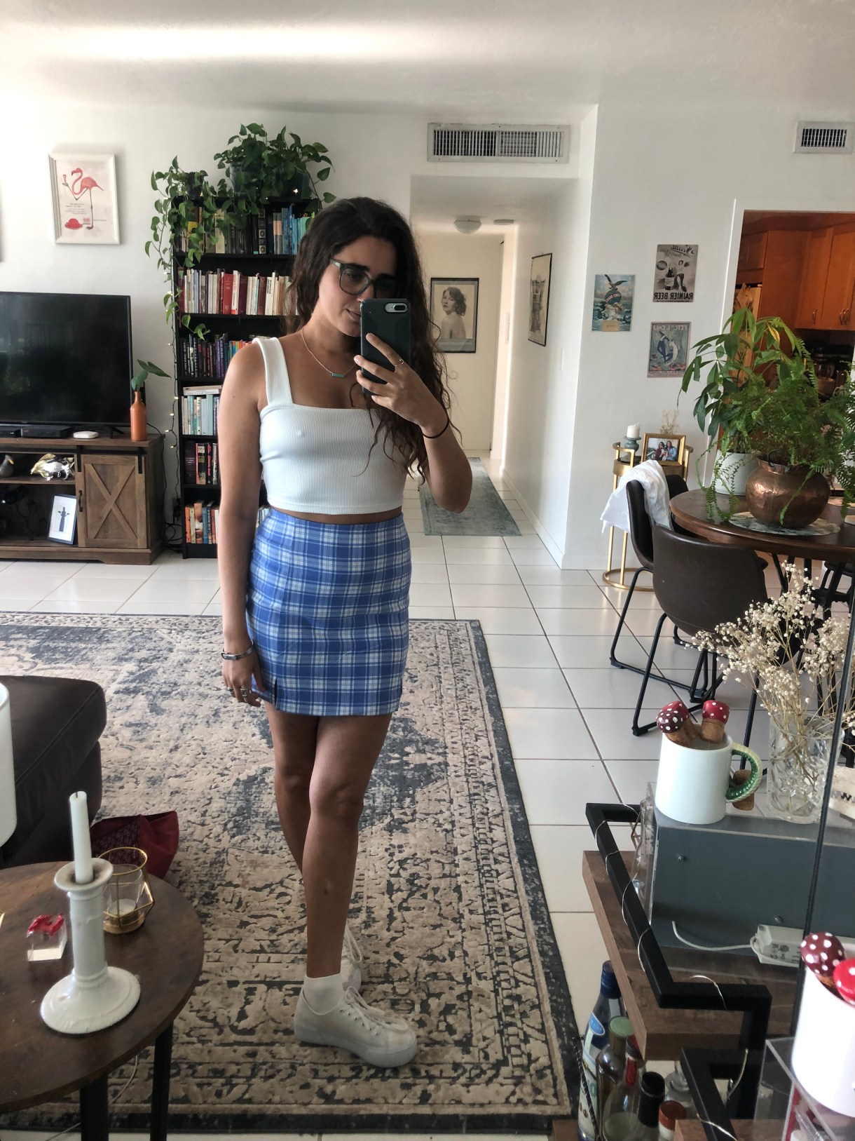 Kayla Kumari Upadhyaya wears a blue and white plaid miniskirt, a white ribbed crop tank with a square neck, a white platform sneakers with white ankle socks.