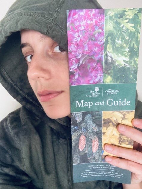 Ro holds up a Botanical Gardens map and guide. Ro is a white human who is in this photo wearing a gray hoodie