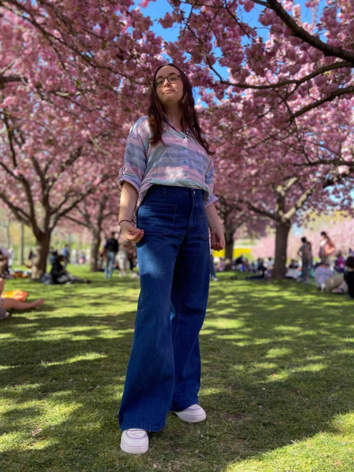 Anya, a white woman with long brown hair, stands in a grove of blossoming trees.