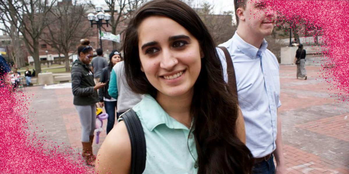 Kayla Kumari Upadhyaya, when she was 22-years-old. Her hair is dark and down, and she's wearing a black backpack and a teal sleeveless buttondown. There's pink glitter on the lower left and upper right corners of the image.