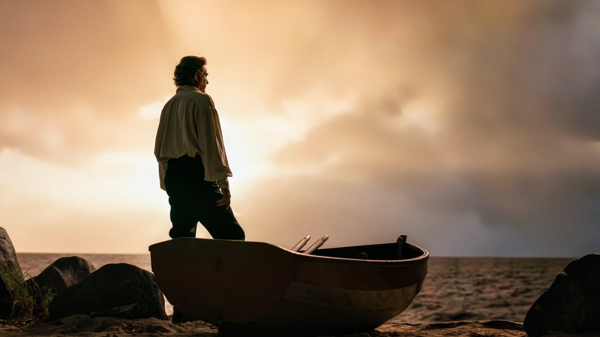 A pirate stands in a row boat and looks out at the setting sun against the ocean