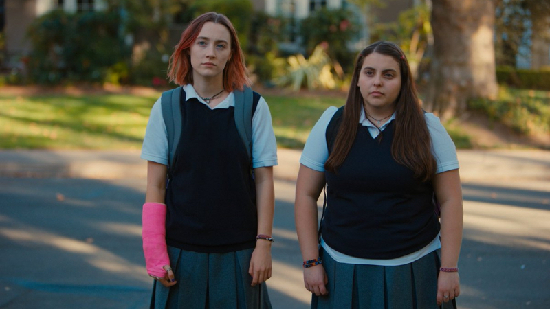 Saoirse Ronan as Lady Bird stands next to Beanie Feldstein as Julie, both in their school uniforms