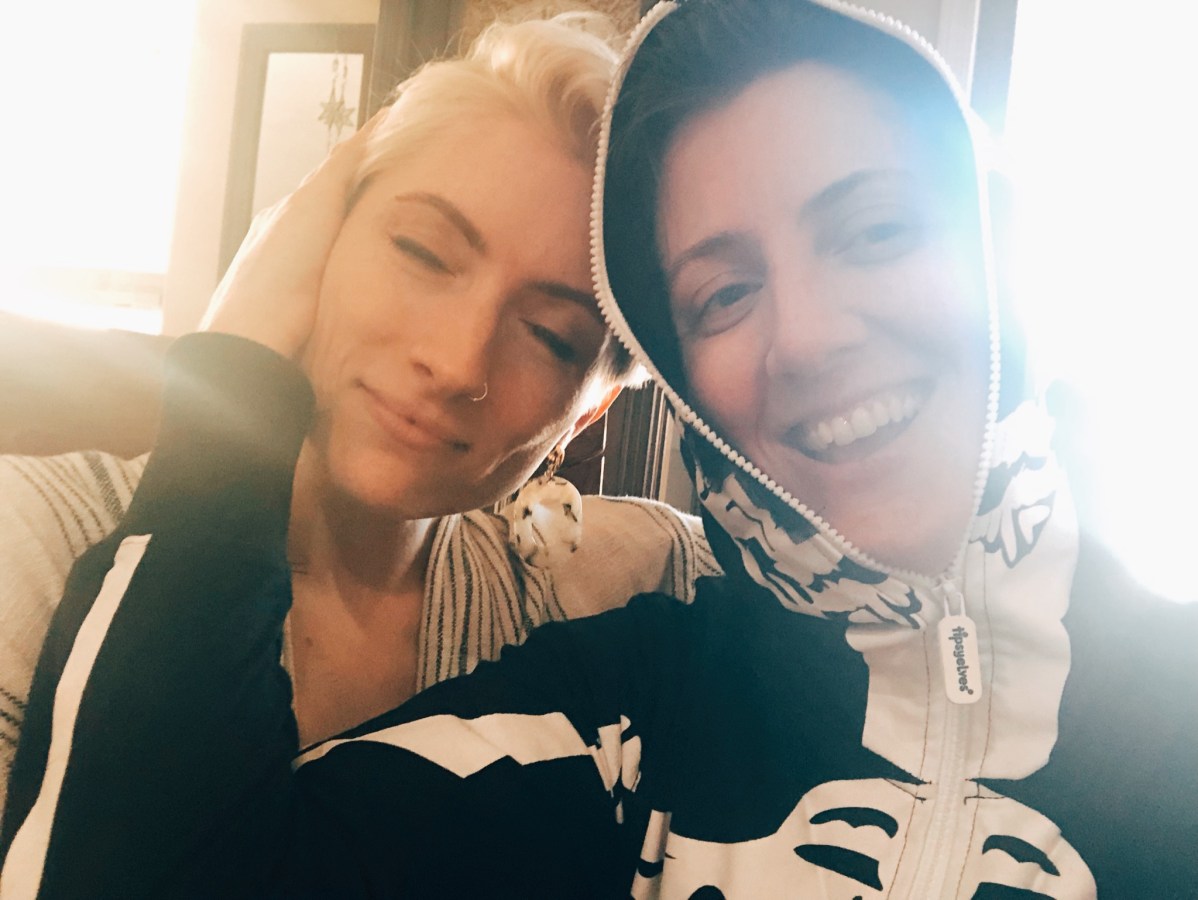 Laneia and Amanda lean against each other. Amanda is smiling and wearing a skeleton hoodie. Laneia is smiling with her eyes closed.