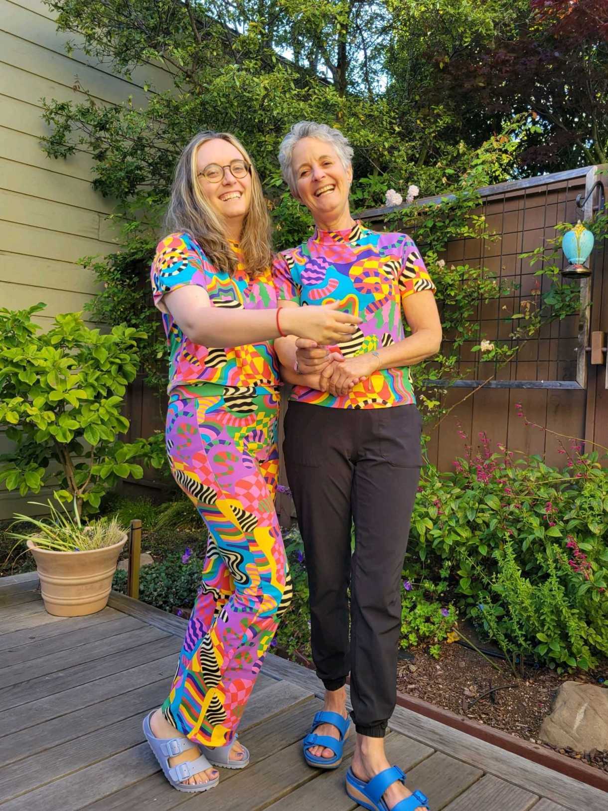 Anya and her mom wear matching outfits with an absolutely WILD PATTERN on them! They both smile and pose for the camera in this full length photo. Anya and her mom are both white women, Anya with long blonde and brown hair and her mom with white and gray short hair. Anya wears glasses.