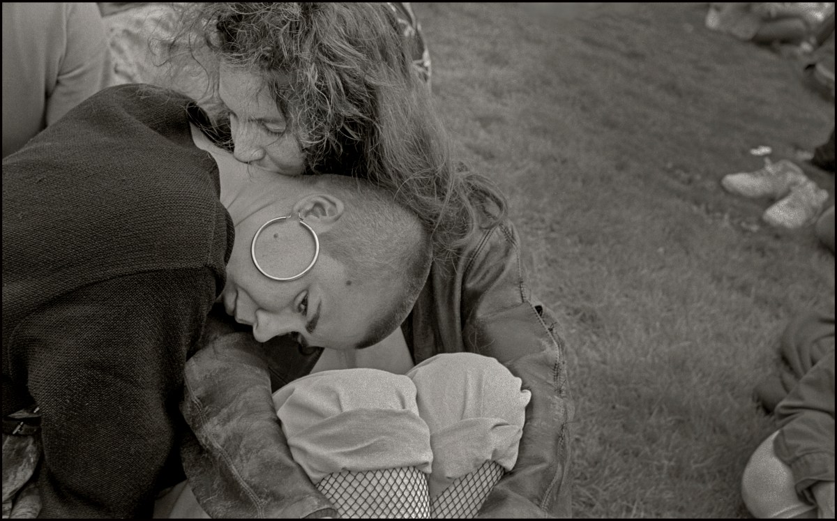 Close-up of two women, one kissing the back of the other's neck. One woman has a buzzcut and large hoop earrings.