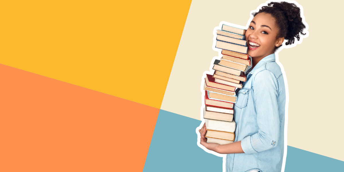 A Black girl with her hair pulled back holds a stack of books while smiling and wearing a buttondown denim shirt