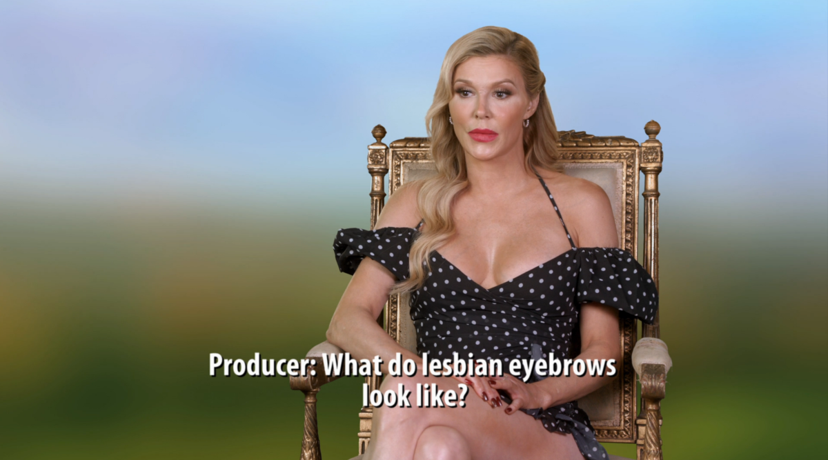 Brandi Glanville, a white woman with blonde hair, wears a black and white polka dot dress. A producer off camera says "What do lesbian eyebrows look like?