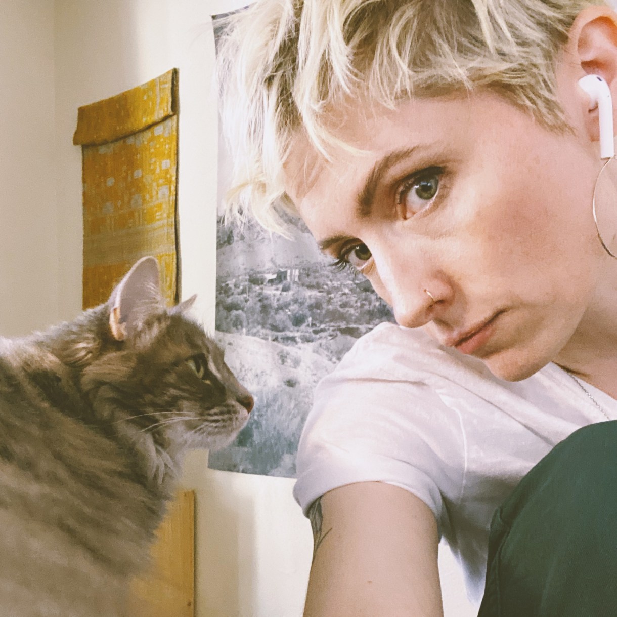 Laneia leans in for a photo with her cat winona. Laneia is a white woman with blonde hair looking directly at the camera. Her hair is short and she is wearing a white tee shirt. The cat is a tabby looking cat.
