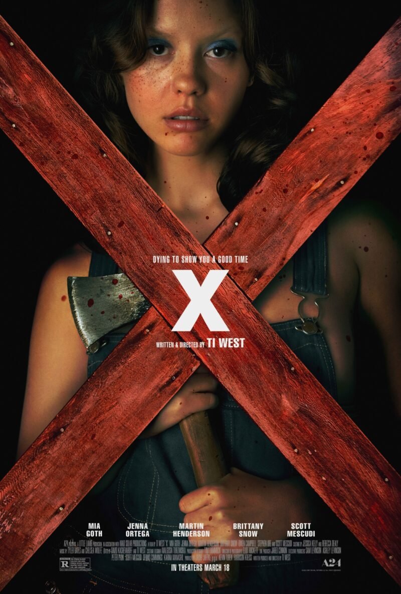 the cover of X shows a gamine-featured human holding an ax, gazing darkly through a crossed x made of red wood boards. this character is played by mia goth.