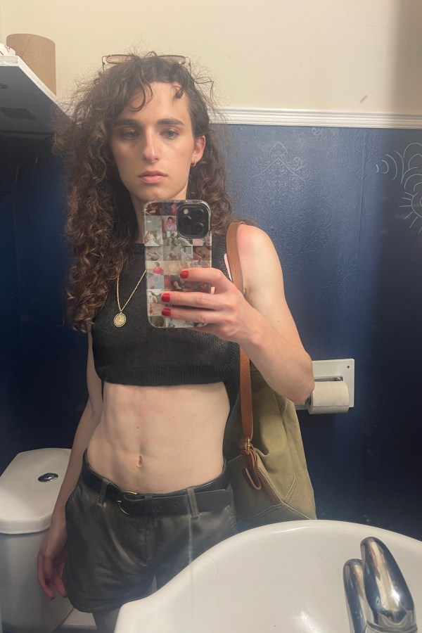 Drew, a white woman, takes a bathroom mirror selfie. She is wearing a short crop top revealing her stomach and is looking at the camera in a devastatingly mean manner. Her hair is long and curly.