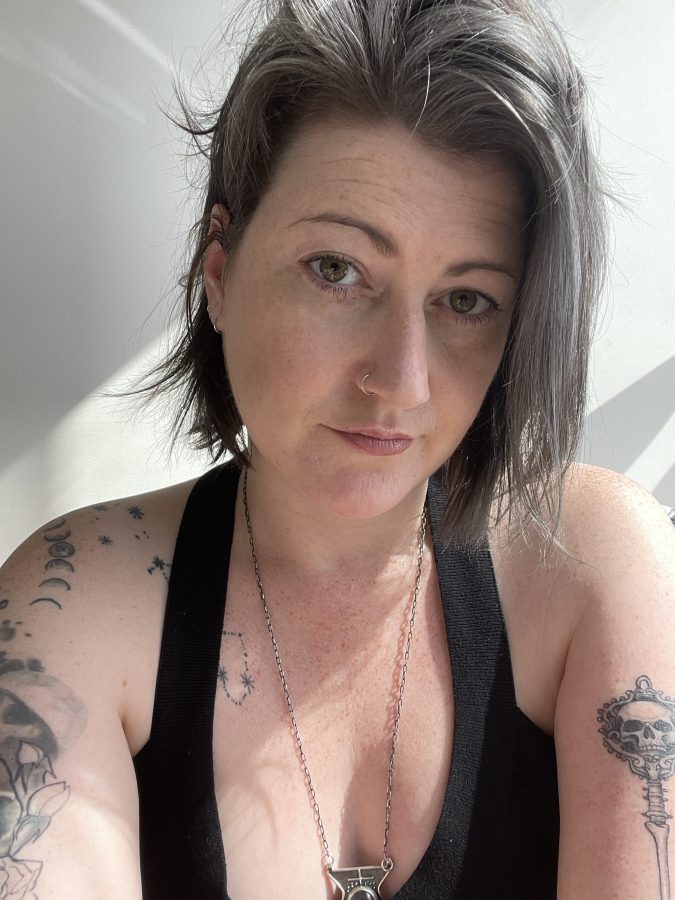 Meg, a white woman, is gazing into the camera, wearing a black tank top. She has a salt and pepper bob.