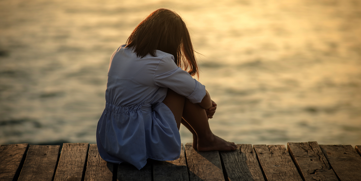 a girl sits all alone, lonely, on the edge of a dock by the water