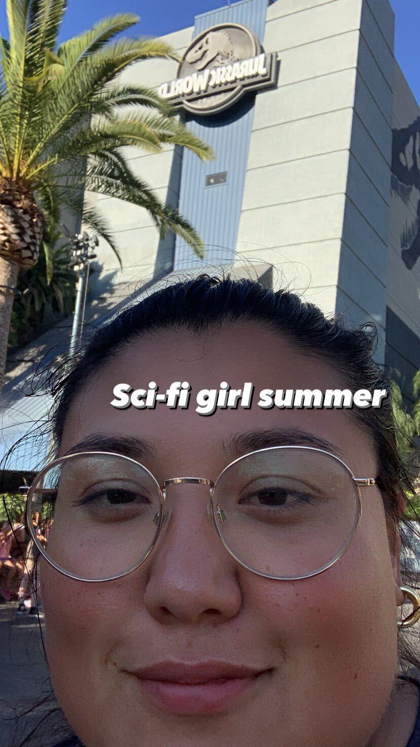 A screenshot of Em Win's Instagram story reading "Sci-fi girl summer" with a close-up of Em Win near a Jurassic Park ride