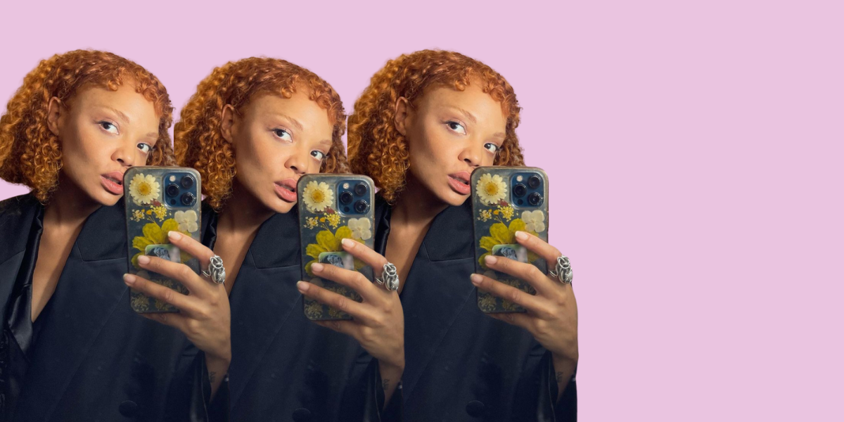 Tessa Thompson with red hair takes a mirror selfie on her iPhone