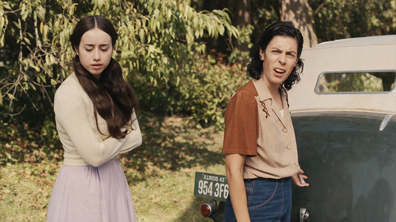 Lupe and Esti stand in front of Sarge's wrecked car. 