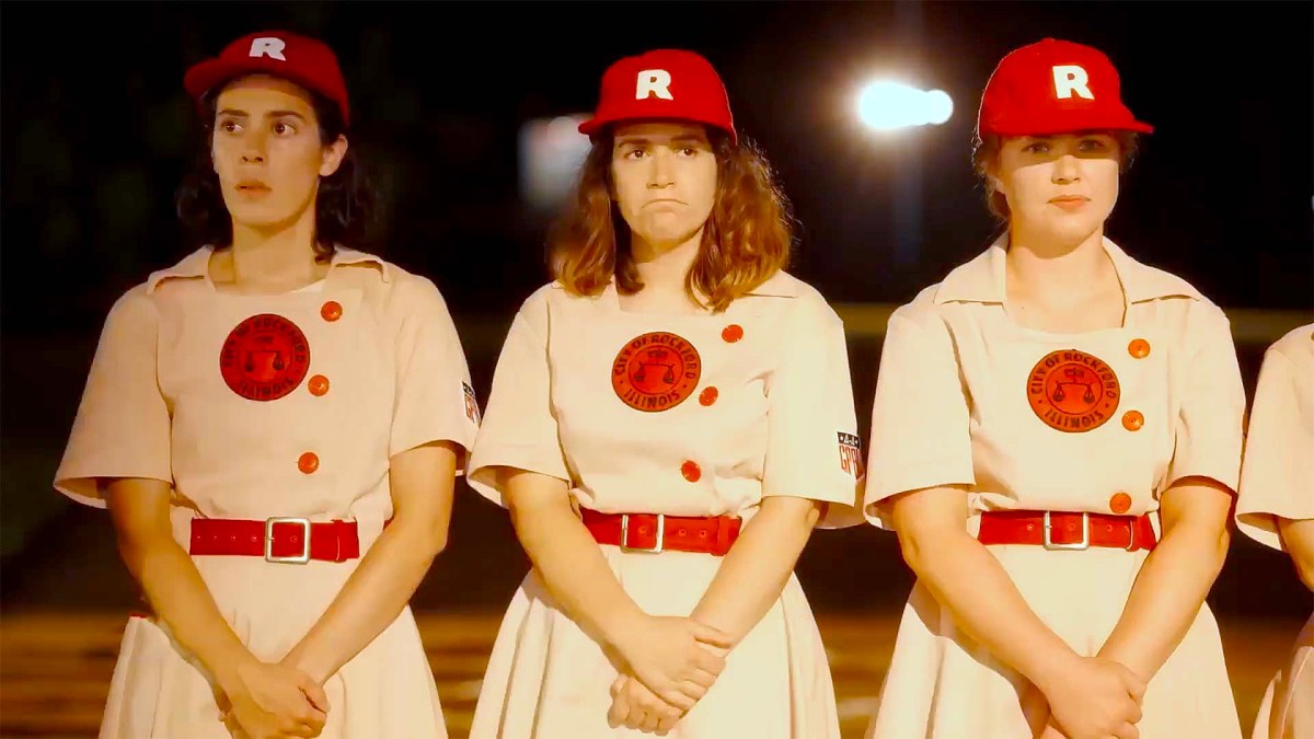 Lupe and Carson standing in bright lights in a dark field in their Rockford Peaches uniforms