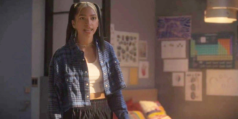 Zaara accuses Junior of stealing her earbuds. She's wearing a blue flannel top over a short white tank top and black pants.