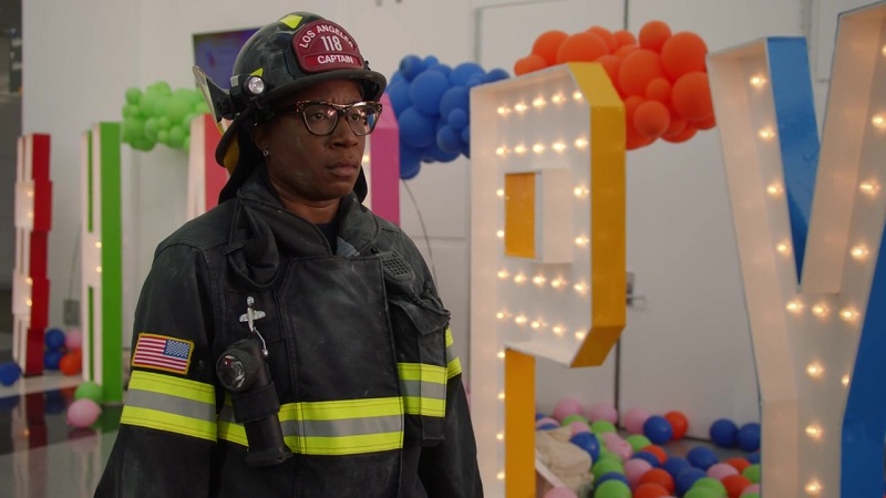 Hen looks despondent after an unsuccessful rescue. She's wearing her firefighter gear (with the Captain's helmet) and walking in front of an illuminated group of letters that spell HAPPY.