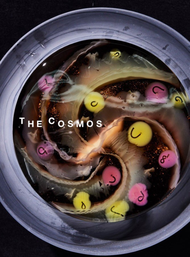 the cosmos jelly cake featuring light starry swirls in a daark background with strange symbols in pink and yellow decorations