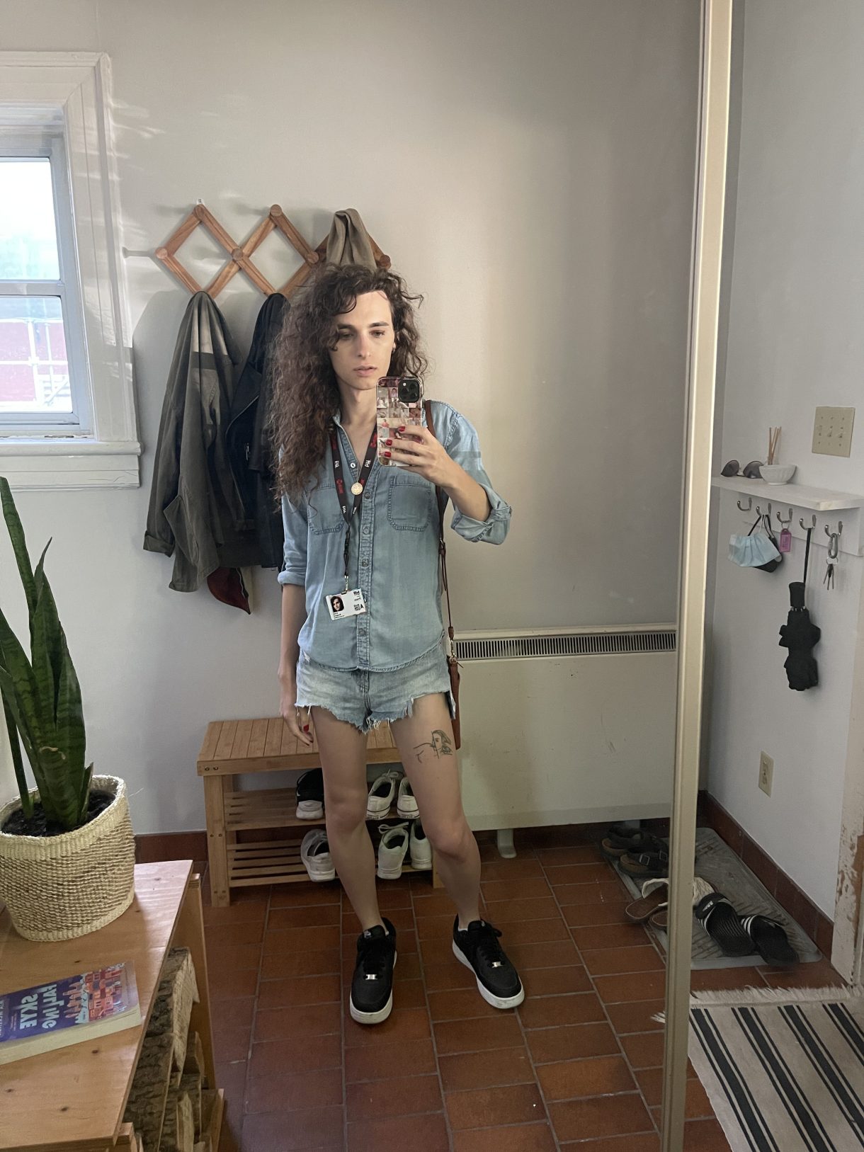 Drew, a white woman with long curly brown hair, stands in a denim shirt, matching denim jorts, sneakers, taking a mirror selfie with her TIFF press pass around her neck