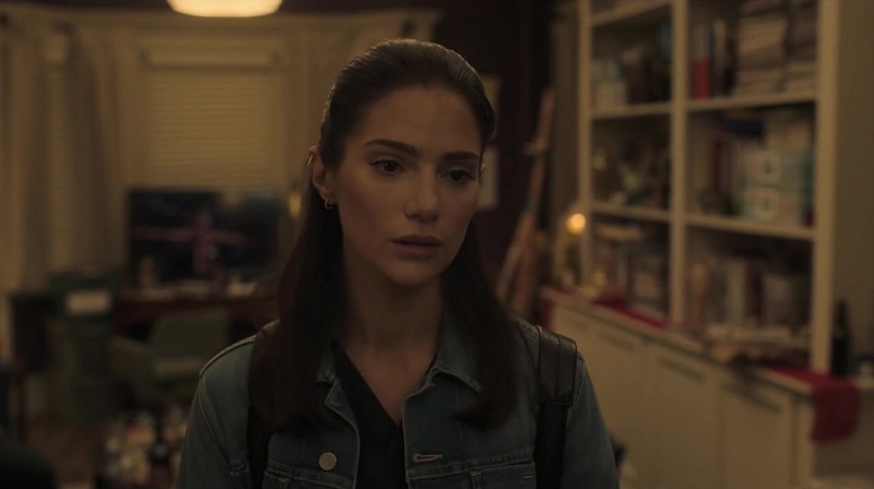 Lauren stands in the middle of her sister's messy apartment. She's wearing a denim jacket and carrying a backpack on both shoulders.