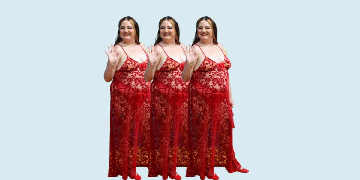 Megan Stalter wears a red sheer lace spaghetti-strap dress to the Emmys with red ballet flats. She waves to the camera while smiling.