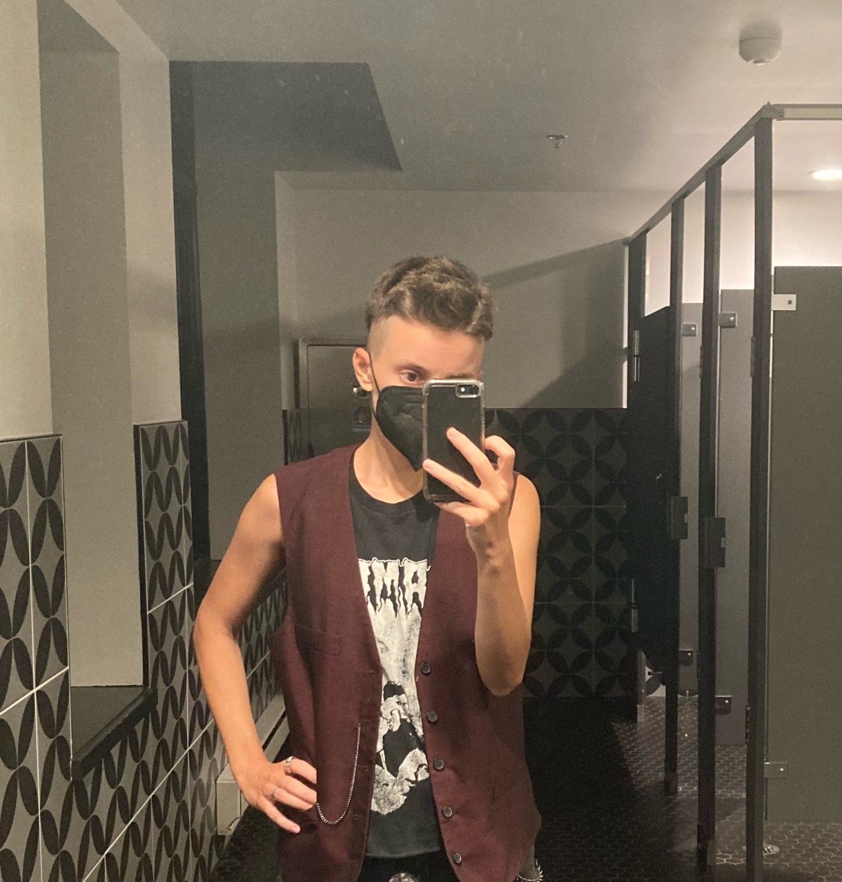 ro a white human stands in a bathroom and takes a mirror selfie, hand on their hip. they have short brown hair, and are wearing a mask, maroon vest and some kind of muscle tee underneath