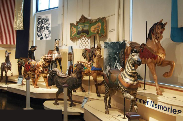 a photo showing a tiger, several horses, a zebra, and a rooster from carousels, each on its own display. they are vintage and old looking, colors and paint faded and strange